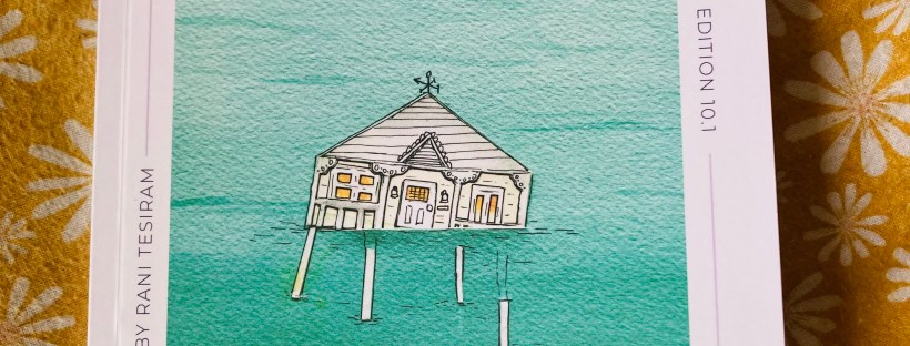 A copy of Jacaranda Journal sitting on a yellow and white floral background. The journal features cover art of a Queenslander house on stilts, partially flooded and surrounded by green-blue water. Around this image is a white border with dark blue text that reads, ‘Jacaranda Journal. Winter 2023. Edition 10.1. Cover art by Rani Tesiram. Poetry. Memoir. Fiction.’